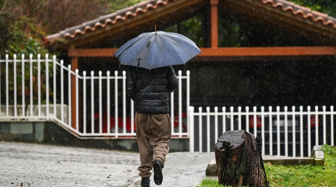 ανδρας περπαταει στη βροχη με ομπρελα
