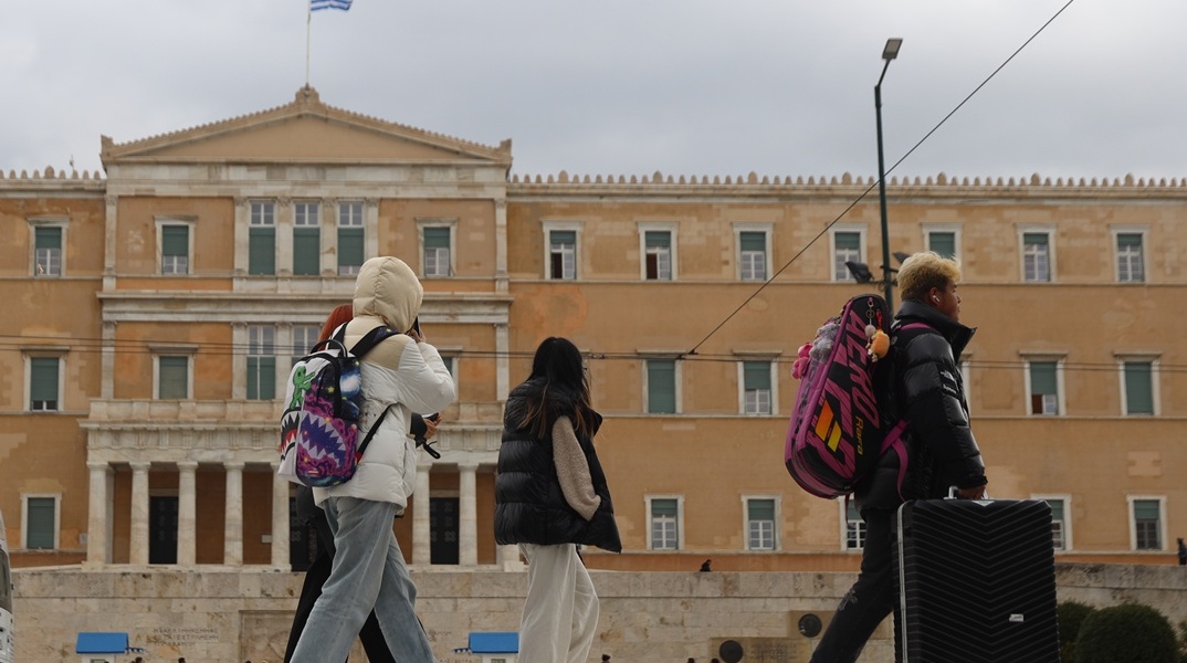 Άτομα με ζεστά ρούχα και μπουφάν περπατούν μπροστά από τη Βουλή