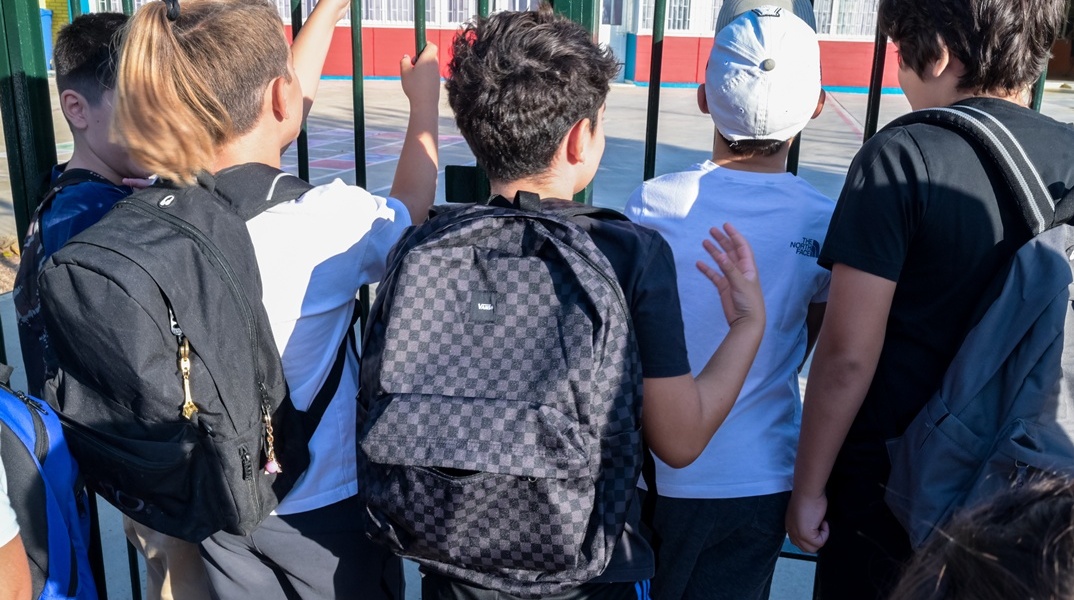 Μαθητές με τις τσάντες τους στην πλάτη αναμένουν να ανοίξει η πόρτα του σχολείου τους
