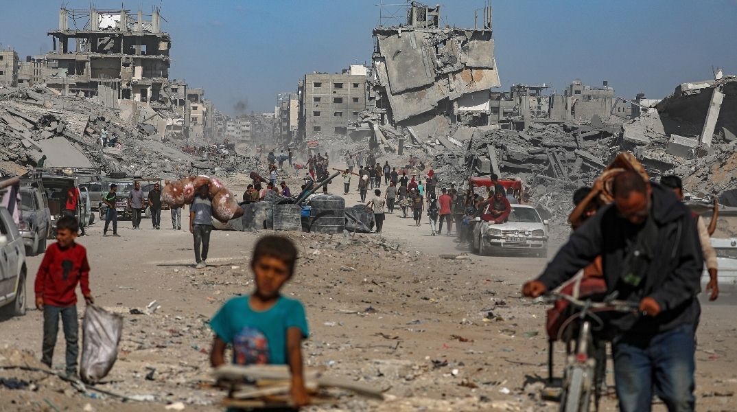 Παλαιστίνιοι περπατούν ανάμεσα σε ερείπια κτιρίων εν μέσω εκεχειρίας μεταξύ Ισραήλ και Χαμάς, στην πόλη της Γάζας