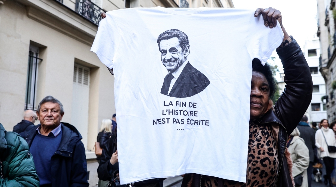 Μια γυναίκα κρατάει ένα μπλουζάκι με το πορτρέτο του πρώην Γάλλου προέδρου Νικολά Σαρκοζί και το μήνυμα «Το τέλος της ιστορίας δεν έχει γραφτεί ακόμα» κατά τη διάρκεια διαδήλωσης κοντά στην κατοικία του πρώην Γάλλου προέδρου την ημέρα που πρόκειται να εισέλθει στη φυλακή