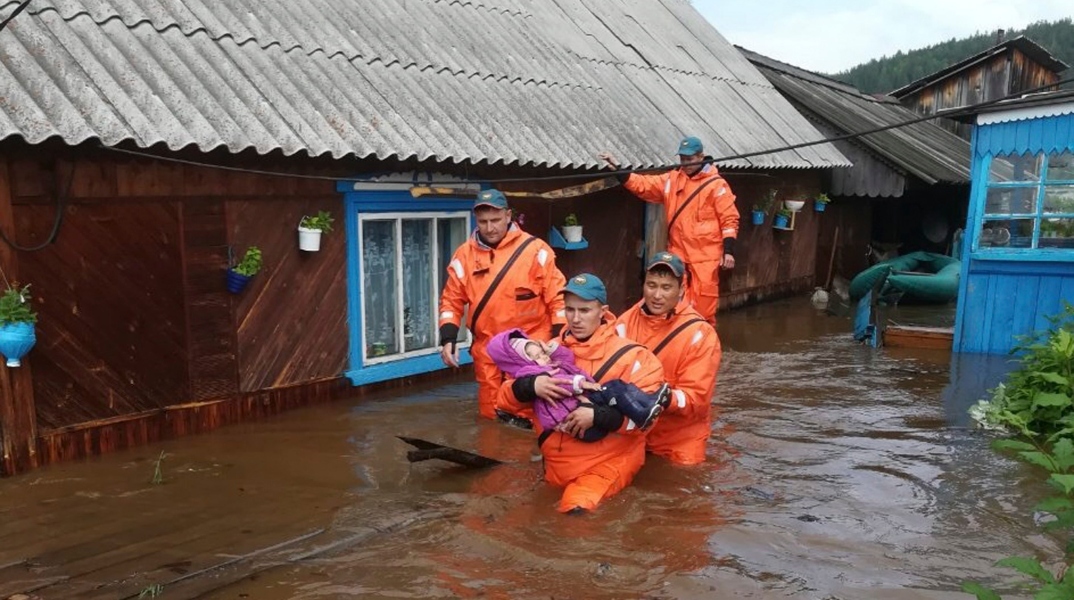 Mέλη του ρωσικού Υπουργείου Έκτακτης Ανάγκης μεταφέρουν ένα παιδί από πλημμυρισμένο σπίτι 