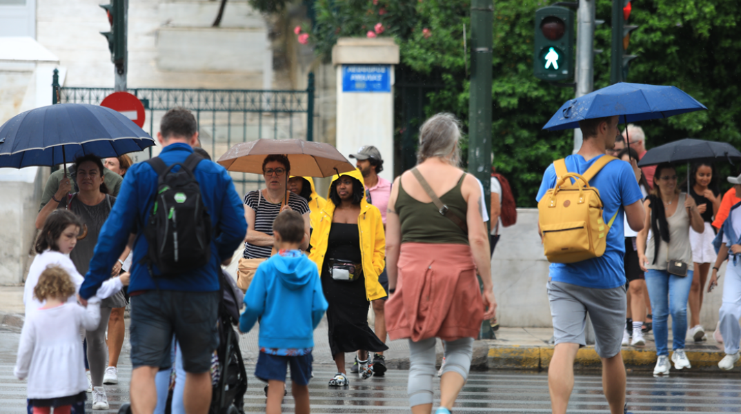 Πολίτες με ομπρέλα περπατούν εν μέσω βροχοπτώσεων