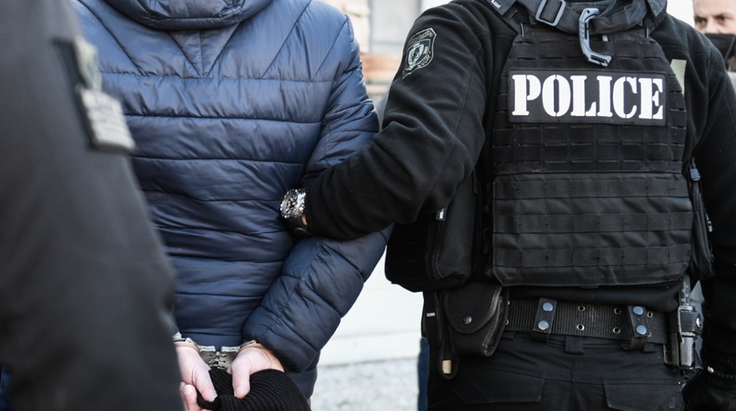Άτομο που φορά χειροπέδες και κρατείται από αστυνομικούς