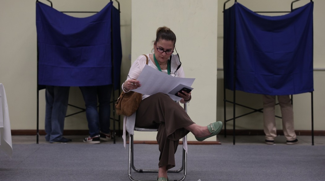 Συνέδριο ΠΑΣΟΚ-ΚΙΝΑΛ: Γυναίκα διαβάζει φυλλάδιο καθισμένη σε καρέκλα ανάμεσα στα δύο παραβάν
