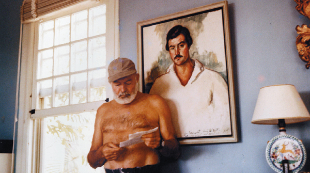 Ο Έρνεστ Χέμινγουεϊ στο σπίτι του στην Κούβα, μπροστά από το πορτρέτο του, περίπου το 1953