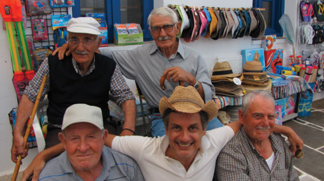 Ο Dimitris Dassios καθισμένος στο παγκάκι ανάμεσα σε φίλους στο νησί