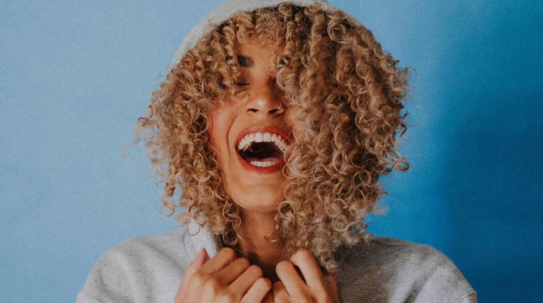 Κοπέλα με σγουρά μαλλιά φοράει κουκούλα και γελάει