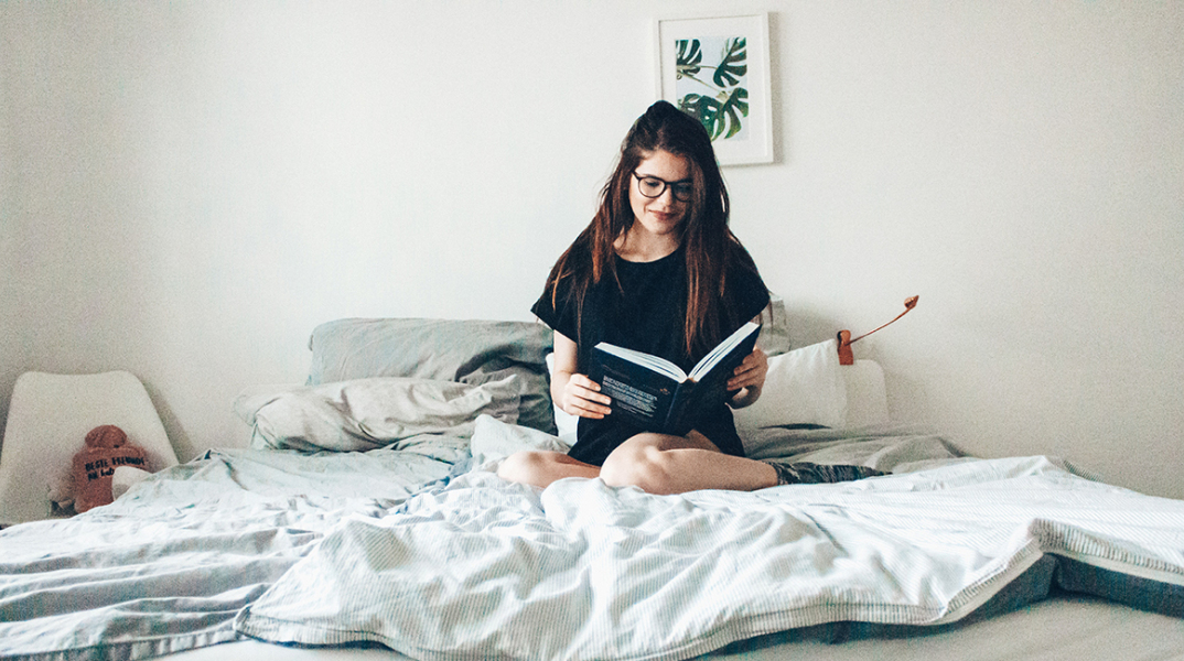 Κοπέλα που κάθεται στο κρεβάτι και διαβάζει βιβλίο