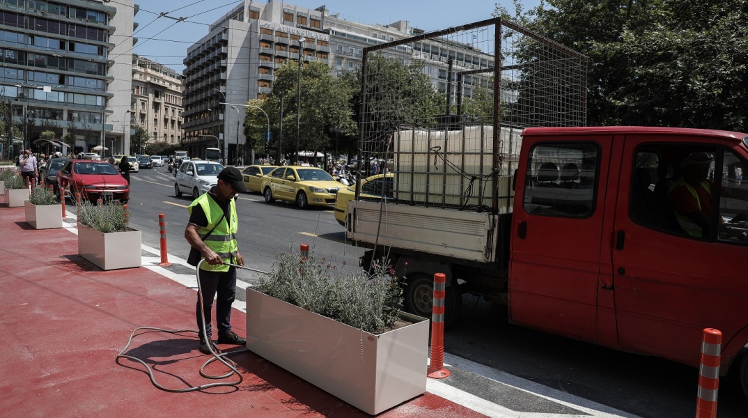 Εργάτης του δήμου ποτίζει λουλούδια σε ζαρντινιέρα στον "Μεγάλο Περίπατο" στο κέντρο της Αθήνας 