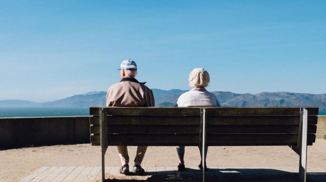 Δύο ηλικιωμένοι κάθονται σε παγκάκι μπροστά από τη θάλασσα