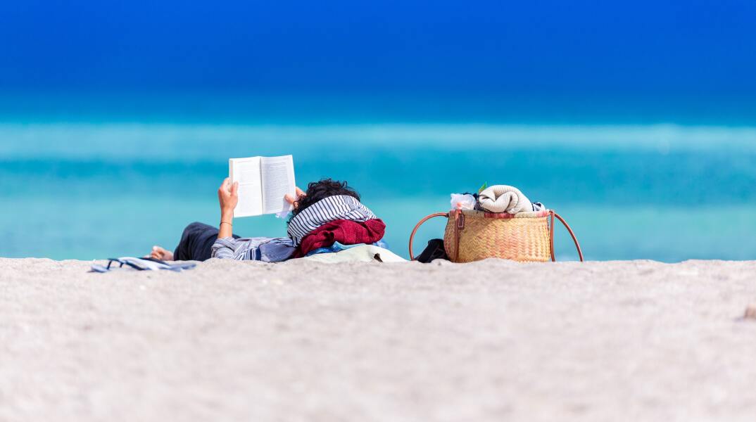 Γυναίκα διαβάζει βιβλίο στην παραλία