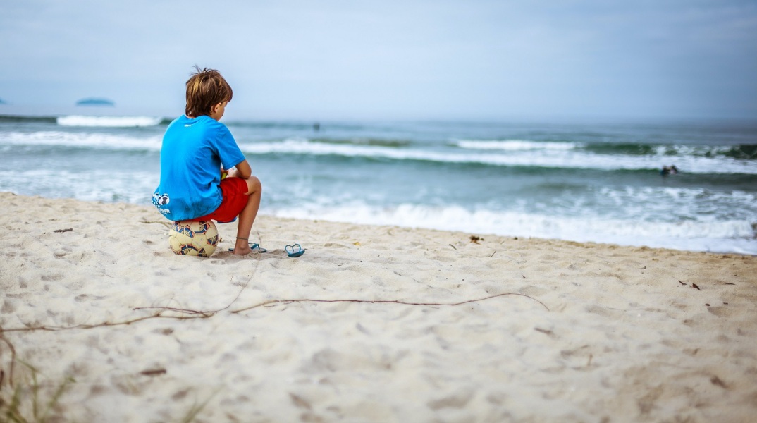 Αγόρι που κάθεται πάνω σε μια μπάλα σε παραλία