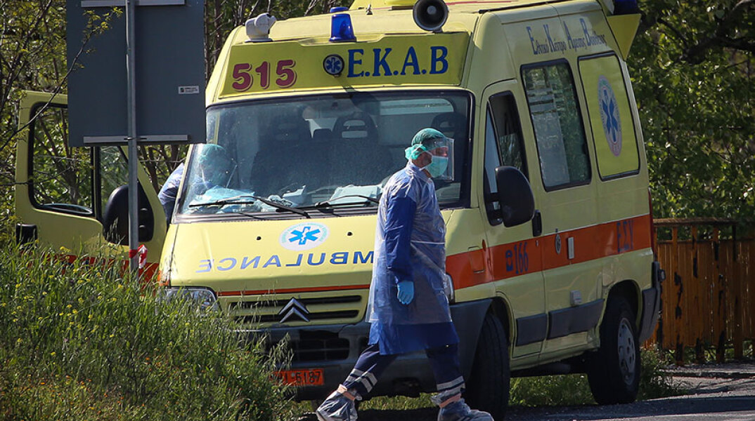 Τραυματιοφορέας με προστατευτική στολή για κορωνοϊό περνά μπροστά από ασθενοφόρο του ΕΚΑΒ