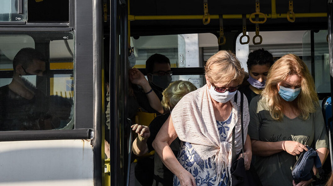 Επιβάτες με μάσκα για τον κορωνοϊό κατεβαίνουν από λεωφορείο στο κέντρο της Αθήνας