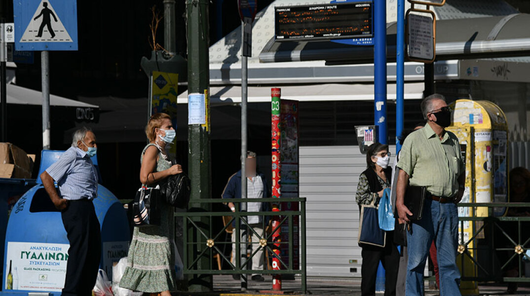 Πολίτες με μάσκα για τον κορωνοϊό περιμένουν το λεωφορείο στη στάση