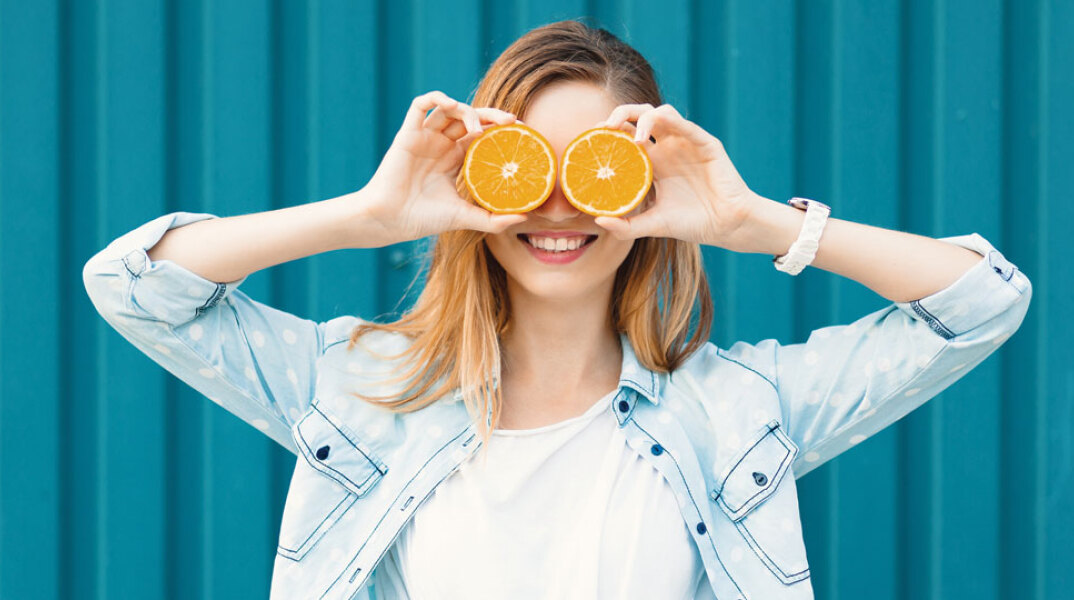 Κορίτσι που κρατάει ροδέλες πορτοκαλιού μπροστά στα μάτια της