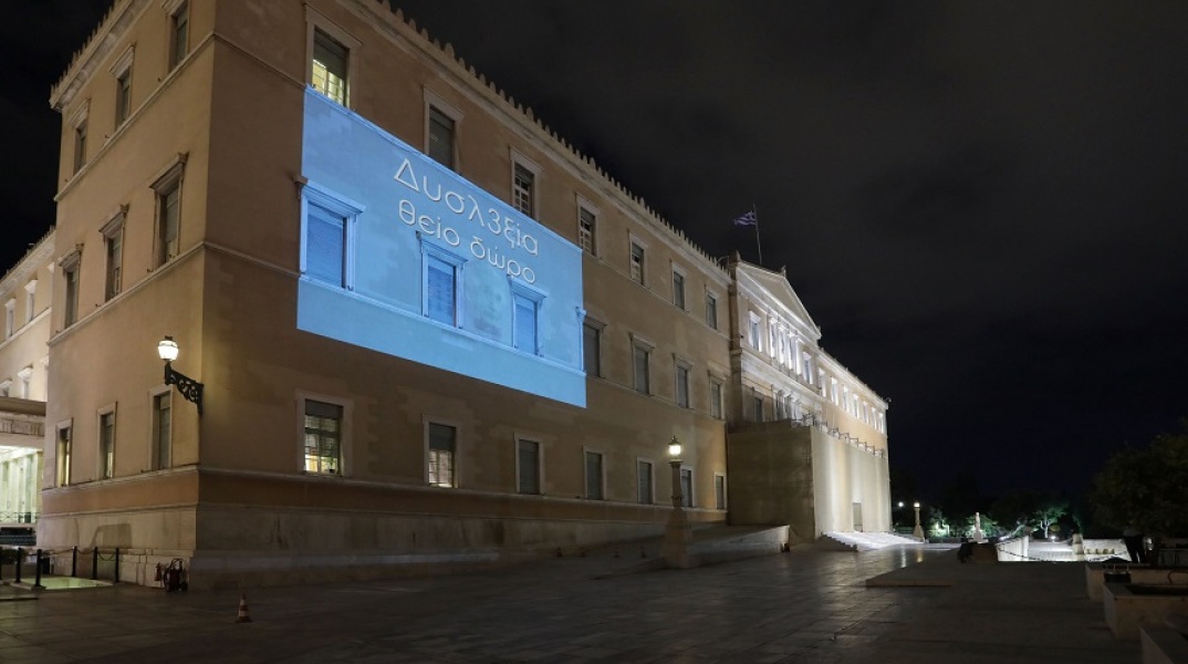 Η πρόσοψη του κτιρίου της Βουλής φωταγωγήθηκε με το σύνθημα «Δυσλ3ξία – Θείο Δώρο»