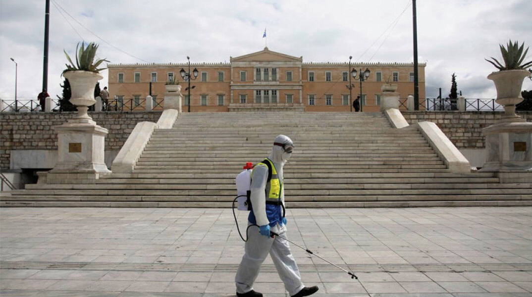 Υπάλληλος του Δήμου Αθηναίων στην πλατεία Συντάγματος με προστατευτική στολή για τον κορωνοϊό