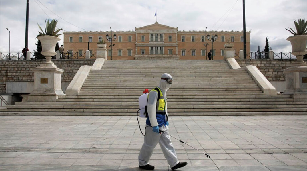 Υπάλληλος του Δήμου Αθηναίων στην πλατεία Συντάγματος με εξοπλισμό απολύμανσης για τον κορωνοϊό