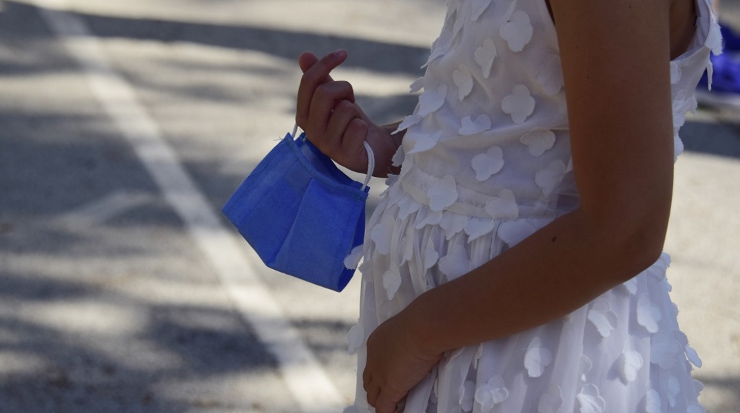 Παιδάκι που κρατά τη μάσκα του στο προαύλιο του σχολείου