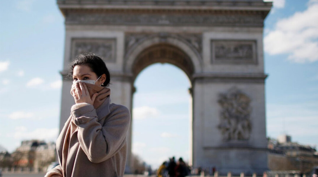 Γυναίκα με μάσκα για τον κορωνοϊό στο Παρίσι με φόντο την Αψίδα του Θριάμβου