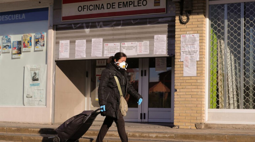 Κορωνοϊός στην Ισπανία: Γυναίκα με προστατευτική μάσκα περνά μπροστά από γραφείο ευρέσεως εργασίας στη Μαδρίτη