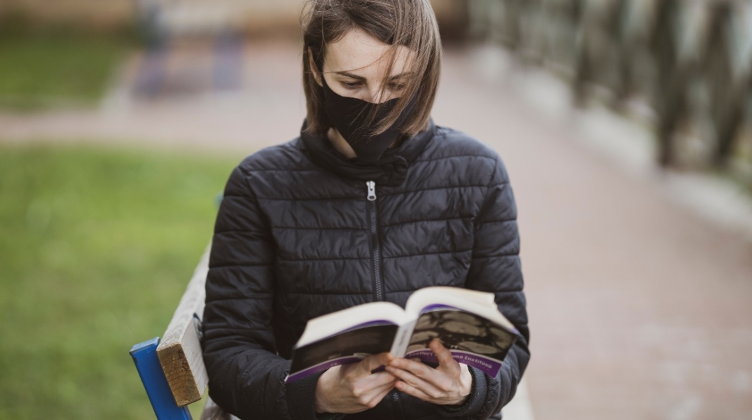 Γυναίκα διαβάζει βιβλίο φορώντας μάσκα