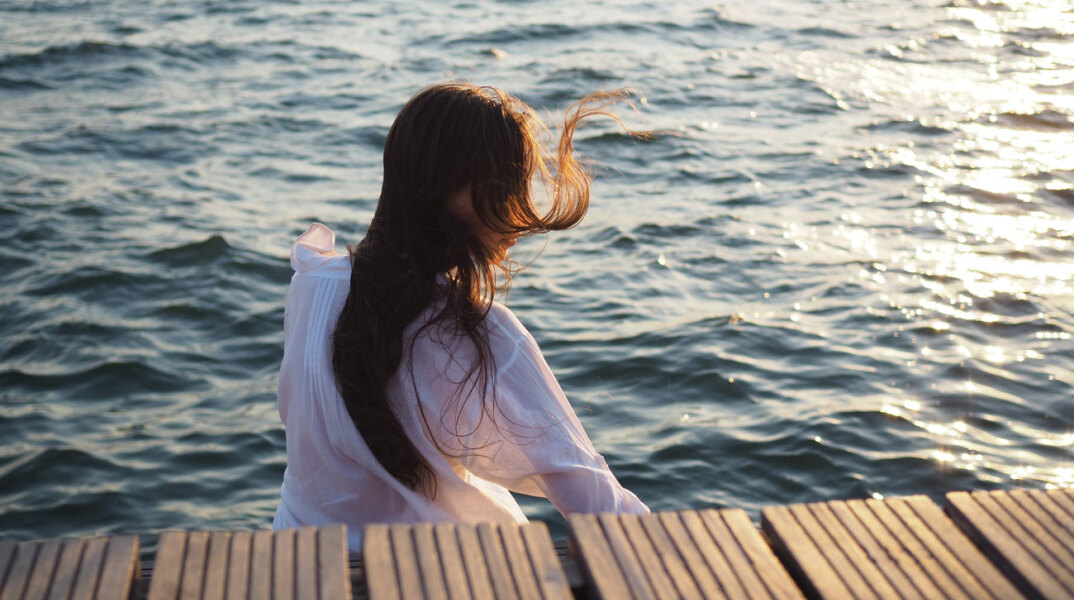 Κορίτσι καθισμένο δίπλα στη θάλασσα με γυρισμένη την πλάτη