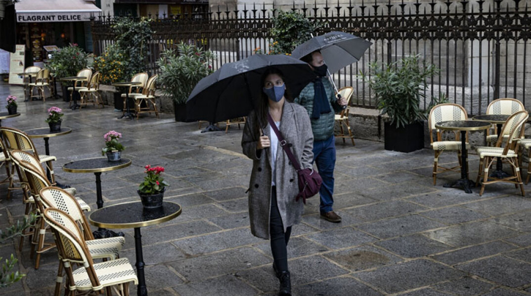 Κορωνοϊός στη Γαλλία: Πολίτες με ομπρέλες περπατούν σε πλακόστρωτο δρόμο στο Παρίσι