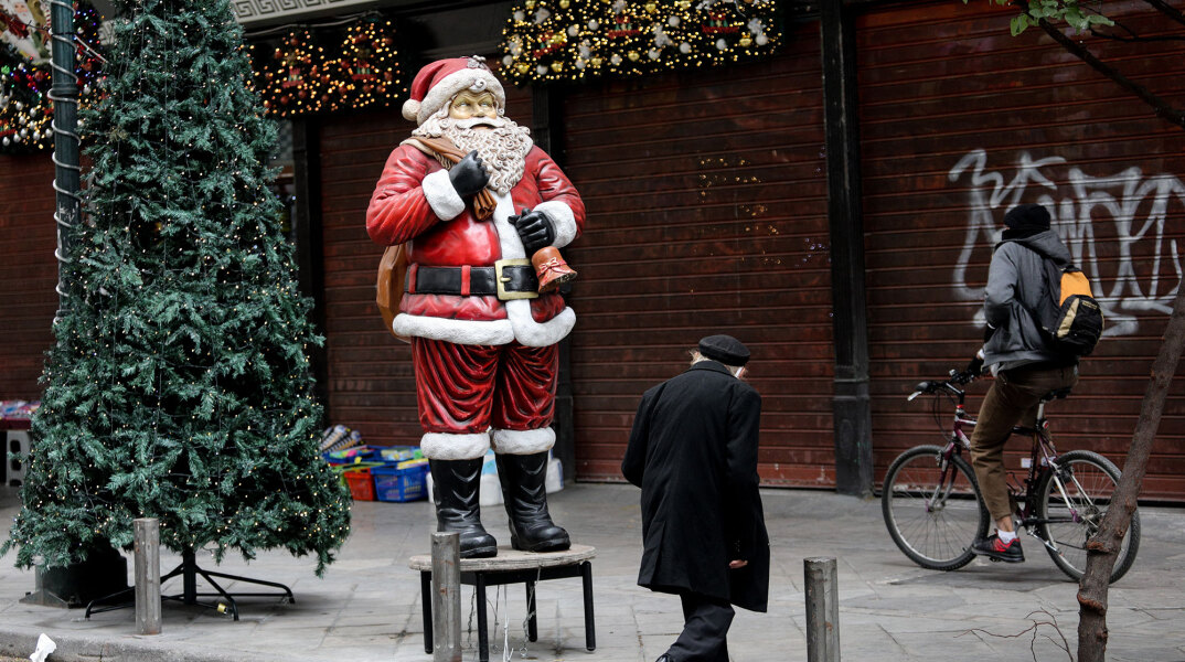 Πολίτες περνούν μπροστά από Άγιο Βασίλη έξω από κλειστά εμπορικά καταστήματα στο κέντρο της Αθήνας εν μέσω lockdown για τον κορωνοϊό