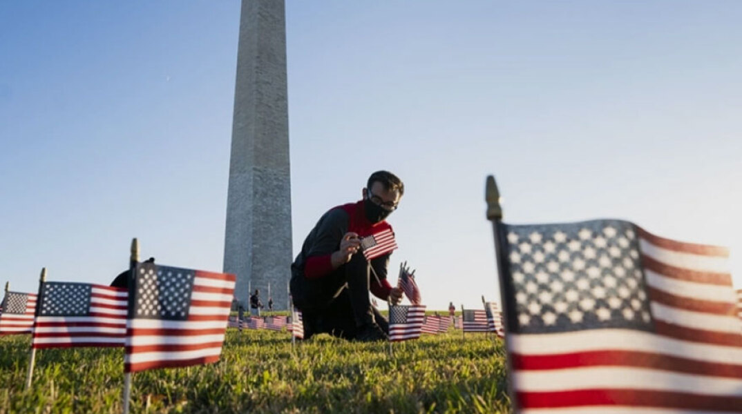 Άνδρας με προστατευτική μάσκα για τον κορωνοϊό τοποθετεί αμερικανικές σημαίες μπροστά από μνημείο στην πρωτεύουσα Ουάσινγκτον