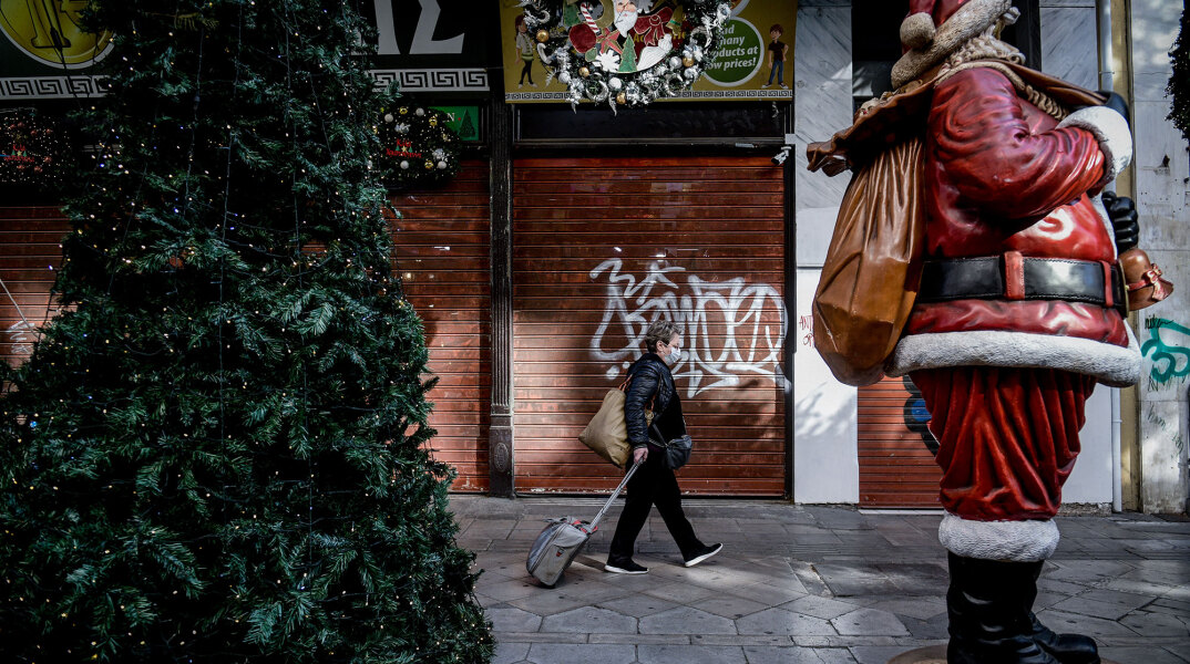 Κορωνοϊός και Χριστούγεννα: Γυναίκα με προστατευτική μάσκα σέρνει βαλίτσα σε πεζόδρομο