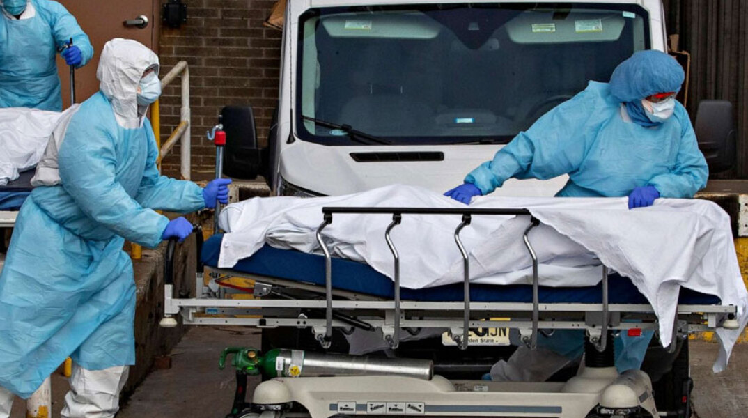Τραυματιοφορείς στις ΗΠΑ με προστατευτικές στολές για τον κορωνοϊό σπρώχνουν φορείο με τη σορό ασθενούς Covid-19