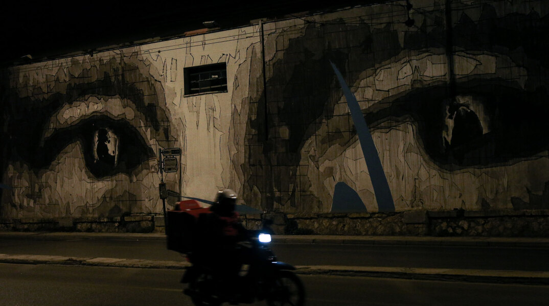 Διανομέας φαγητού περνά με το μηχανάκι μπροστά από τοιχογραφία σε κεντρικό δρόμο της Αθήνας εν μέσω lockdown για τον κορωνοϊό