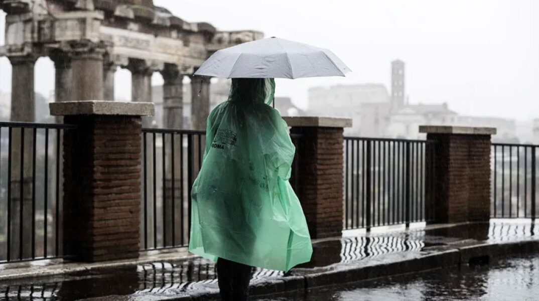 Τουρίστρια με ομπρέλα και αδιάβροχο έξω από τη Ρωμαϊκή Αγορά