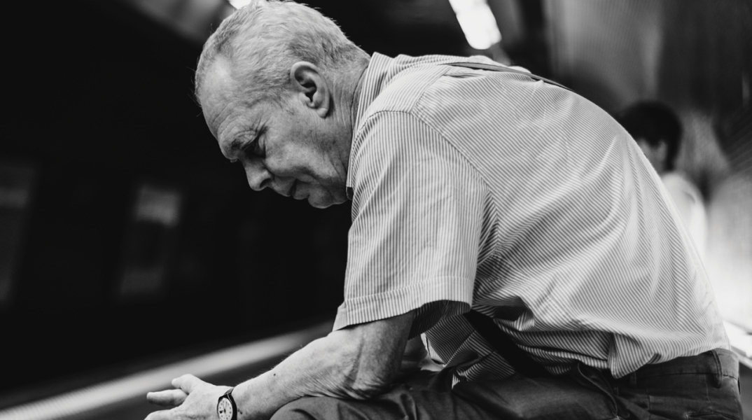 Ασπρόμαυρη φωτογραφία καθιστού ηλικιωμένου άνδρα σε σταθμό μετρό