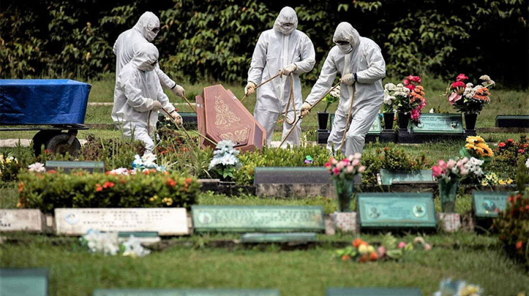 Με προστατευτικές στολές για τον κορωνοϊό, υπάλληλοι γραφείου τελετών στο Σάο Πάολο στη Βραζιλία κατεβάζουν με σχοινιά το φέρετρο νεκρού