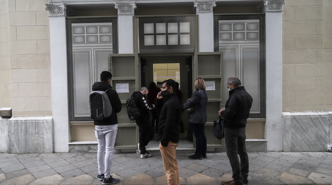 Πολίτες φορώντας μάσκα αναμένουν έξω από τράπεζα