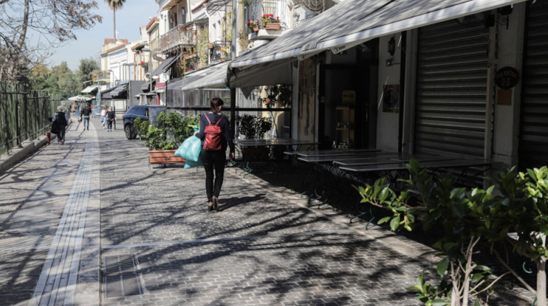 Γυναίκα με τσάντα στην πλάτη περπατά σε πεζόδρομο στο κέντρο της Αθήνας με φόντο τα κλειστά μαγαζιά εν μέσω lockdown
