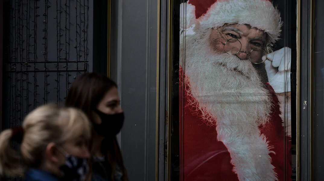 Πολίτες με μάσκα για τον κορωνοϊό στη Θεσσαλονίκη με φόντο εικόνα του Άγιου Βασίλη