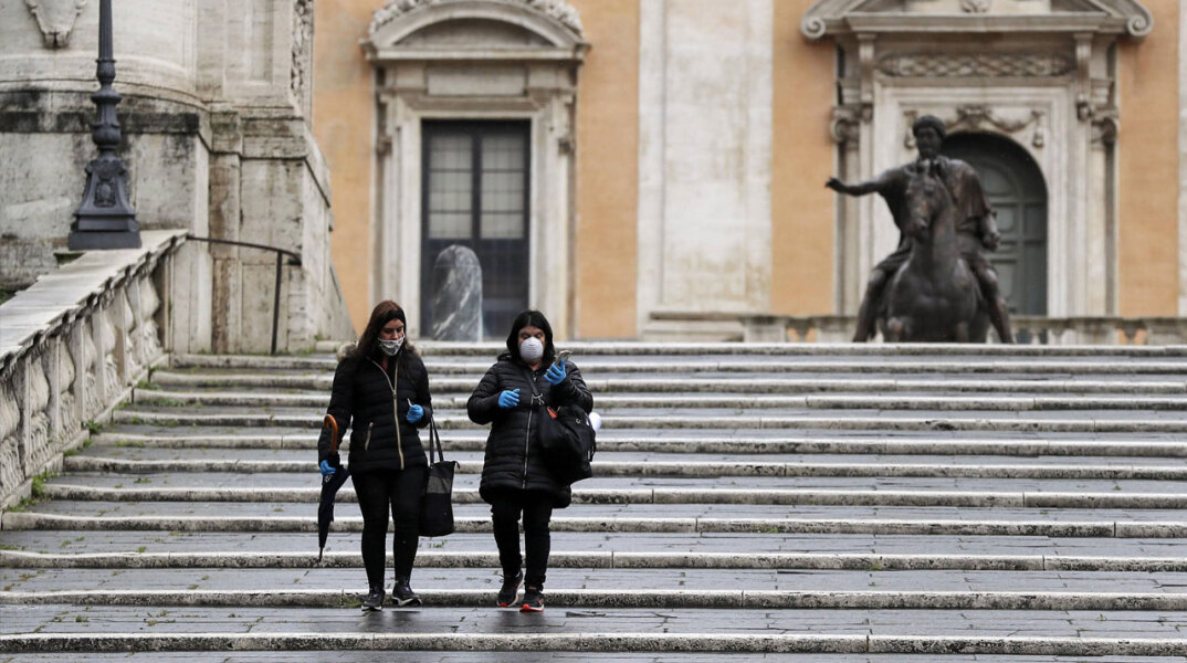 Γυναίκες με προστατευτική μάσκα για τον κορωνοϊό κατεβαίνουν τις σκάλες στο Καπιτώλιο με φόντο το άγαλμα του Μάρκου Αυρηλίου