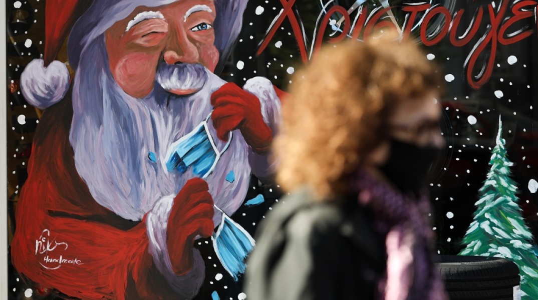 Γυναίκα με μάσκα μπροστά από χριστουγεννιάτικη βιτρίνα