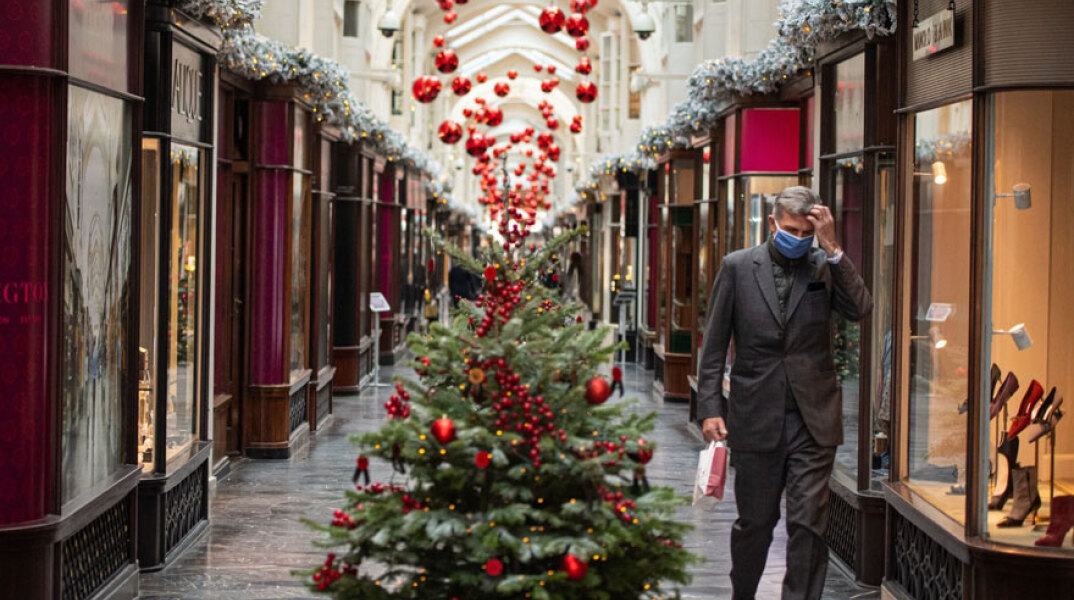 Άνδρας με προστατευτική μάσκα για τον κορωνοϊό περνά δίπλα από χριστουγεννιάτικο δέντρο στο Λονδίνο