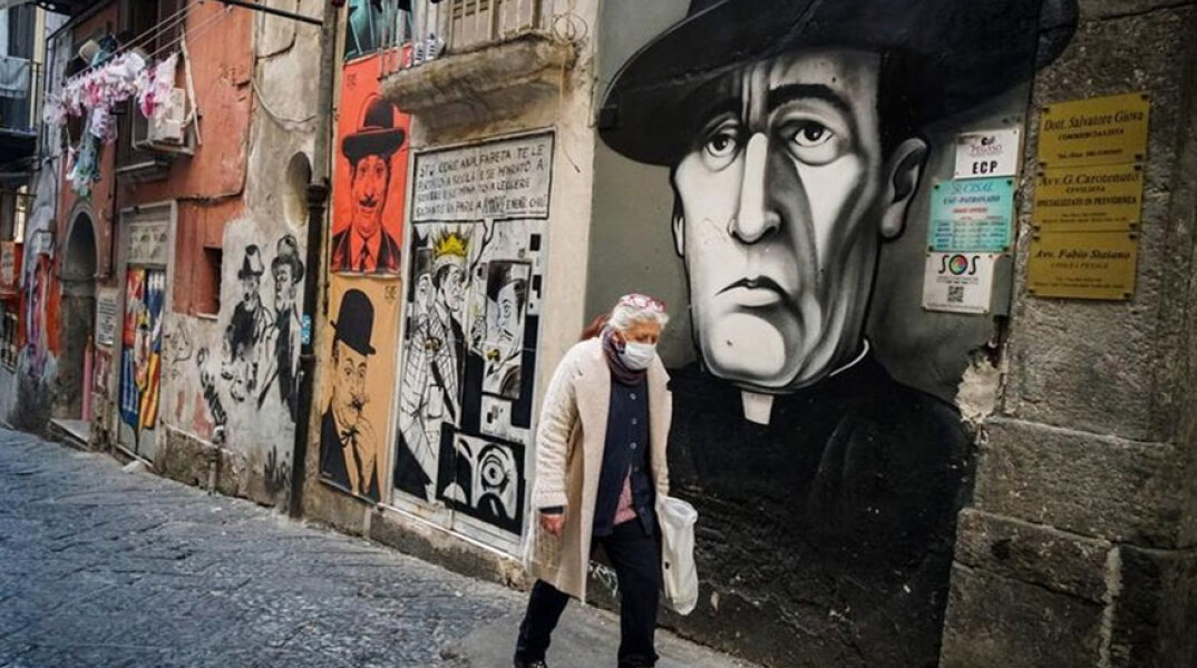Ιταλία - Covid-19: Άνδρας με προστατευτική μάσκα για τον κορωνοϊό περνά μπροστά από γκράφιτι