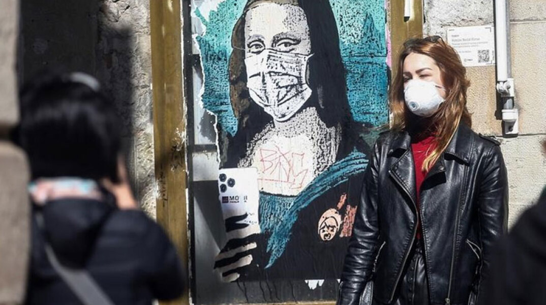 Γυναίκα με προστατευτική μάσκα για τον κορωνοϊό περνά μπροστά από γκράφιτι με την Τζοκόντα