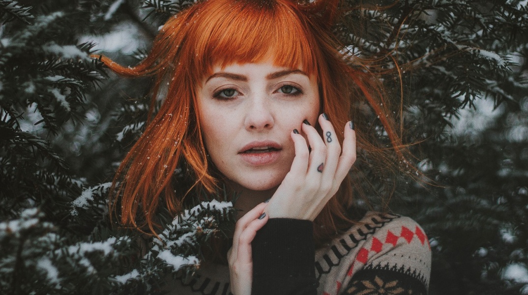 Γυναίκα με κόκκινα μαλλιά που ποζάρει πίσω από χιονισμένο δέντρο
