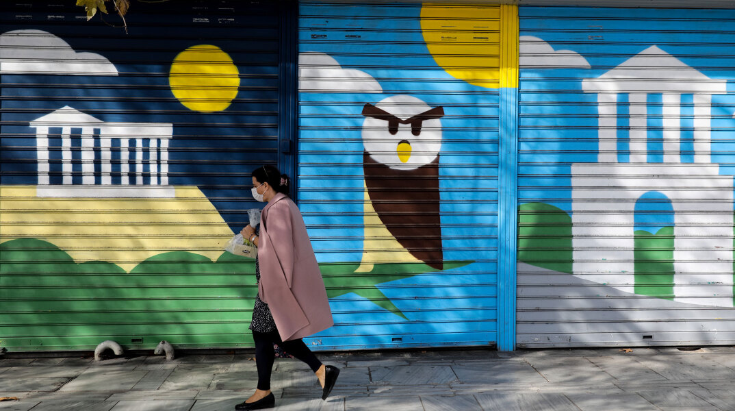 Lockdown στην Αττική για τον κορωνοϊό: Γυναίκα με μάσκα περνά μπροστά από γκράφιτι στο κέντρο της Αθήνας