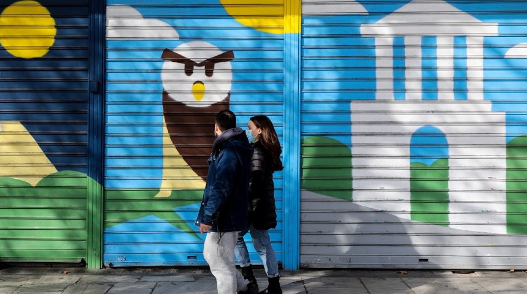 Πολίτες με μάσκα περπατούν μπροστά από κλειστά καταστήματα