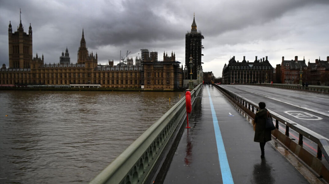 Γυναίκα με μάσκα για τον κορωνοϊό διασχίζει τη γέφυρα Westminster στο Λονδίνο εν μέσω lockdown για τον κορωνοϊό